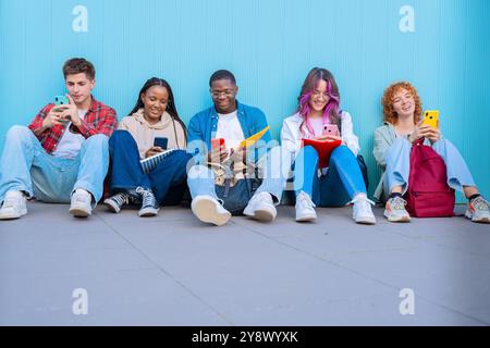 Un gruppo di giovani diversi seduti all'aperto utilizzando smartphone e notebook Foto Stock