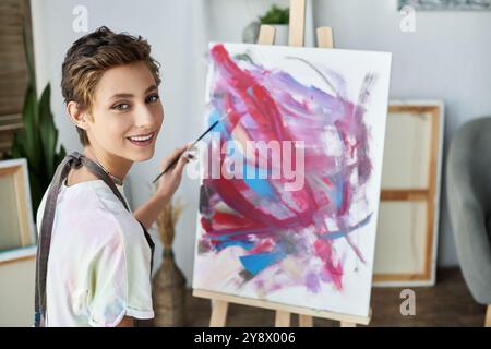 Una giovane donna con trucco naturale ama dipingere su tela, esprimendo il suo lato artistico nella sua accogliente casa. Foto Stock