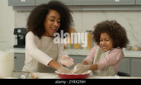 Amata mamma afroamericana felice che insegna carina figlia di bambino che impara impastare l'impasto divertente figlia di famiglia che aiuta la madre a preparare i biscotti cucinare Foto Stock