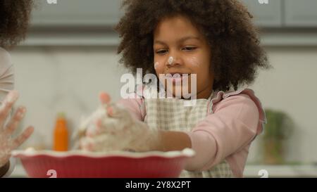 Famiglia afroamericana che cucina felice divertente faccia sporca figlia impastare l'impasto con la donna madre irriconoscibile insegnare bambino bambina cucinare il pane Foto Stock