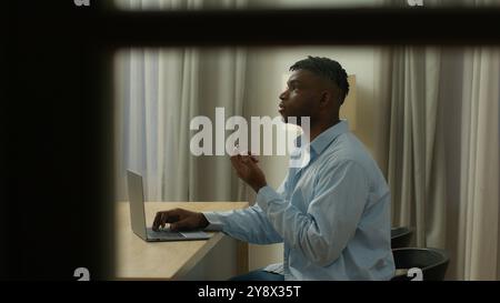Punto di vista spia POV uomo afroamericano ragazzo utente maschio libero professionista studente uomo d'affari lavoro sera a casa pensando pensivo Foto Stock