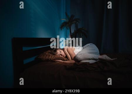 Una donna anziana che si è svegliata nel bel mezzo della notte a causa di un incubo o di un attacco di panico giace accarezzata sul suo letto nella sua camera da letto, spaventata. Copia sp Foto Stock