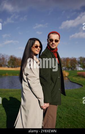 Una coppia gode di un momento tenero, mano nella mano, vestito con caldo abbigliamento autunnale vicino a un tranquillo laghetto. Foto Stock