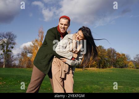 Una coppia condivide un momento d'amore indossando comodi abiti autunnali, circondati da un vivace fogliame autunnale. Foto Stock