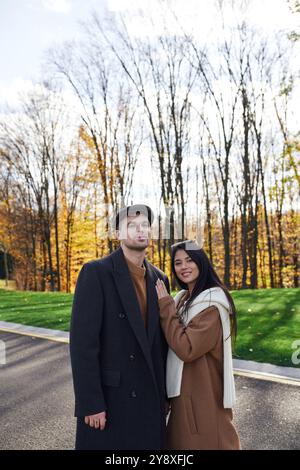 Una coppia abbraccia un intimo abbigliamento autunnale, circondato da un vivace fogliame autunnale sotto un cielo luminoso. Foto Stock