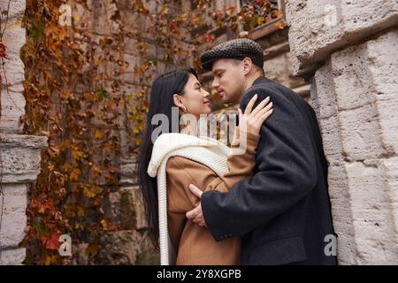 Una coppia si gode un momento tenero con un caldo abbigliamento autunnale in mezzo a un colorato fogliame autunnale. Foto Stock