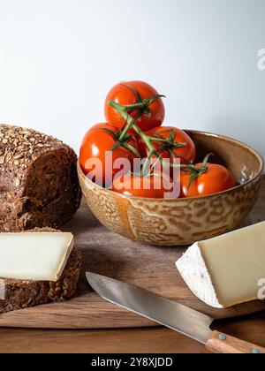 Pomodori freschi, formaggio francese, pane integrale su una tavola di legno rustica con un coltello lucido Foto Stock