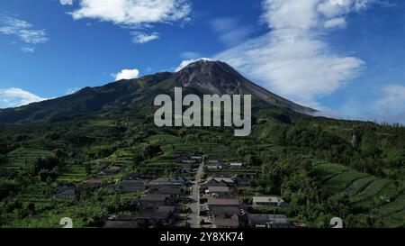 Vista sui droni, le case nel villaggio di Stabelan circondate dall'agricoltura. Il maestoso Monte Merapi offre uno splendido sfondo con un cielo blu nuvoloso Foto Stock