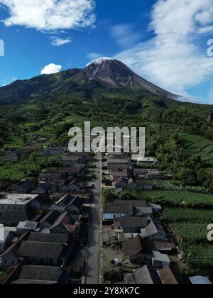Drone verticale, le case nel villaggio di Stabelan circondate dall'agricoltura. Il maestoso Monte Merapi offre uno splendido sfondo con un cielo blu nuvoloso Foto Stock