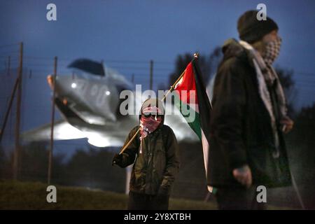 Blackburn, Inghilterra, Regno Unito. 7 ottobre 2024. I manifestanti si riuniscono su un modello di jet da combattimento vicino al cancello principale durante la dimostrazione. I manifestanti bloccano tutti e quattro i cancelli e negano l'accesso al personale della BAE Systems di Samlesbury. La protesta segna il primo anniversario dell'inizio della guerra Gaza/Israele, che ha visto oltre 41.000 civili uccisi. I manifestanti accusano BAE Systems di essere complice del genocidio di Gaza producendo i caccia F-35 nella loro struttura di Samlesbury. Crediti: ZUMA Press, Inc./Alamy Live News Foto Stock