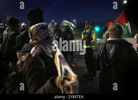 Blackburn, Inghilterra, Regno Unito. 7 ottobre 2024. Un agente di polizia spiega con i manifestanti di cercare di convincerli a lasciare la strada al cancello principale durante la dimostrazione. I manifestanti bloccano tutti e quattro i cancelli e negano l'accesso al personale della BAE Systems di Samlesbury. La protesta segna il primo anniversario dell'inizio della guerra Gaza/Israele, che ha visto oltre 41.000 civili uccisi. I manifestanti accusano BAE Systems di essere complice del genocidio di Gaza producendo i caccia F-35 nella loro struttura di Samlesbury. Crediti: ZUMA Press, Inc./Alamy Live News Foto Stock