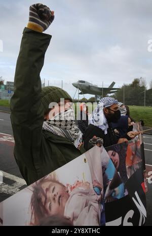 Blackburn, Inghilterra, Regno Unito. 7 ottobre 2024. Un manifestante pugni l'aria in sfida da dietro uno striscione durante la dimostrazione. I manifestanti bloccano tutti e quattro i cancelli e negano l'accesso al personale della BAE Systems di Samlesbury. La protesta segna il primo anniversario dell'inizio della guerra Gaza/Israele, che ha visto oltre 41.000 civili uccisi. I manifestanti accusano BAE Systems di essere complice del genocidio di Gaza producendo i caccia F-35 nella loro struttura di Samlesbury. Crediti: ZUMA Press, Inc./Alamy Live News Foto Stock