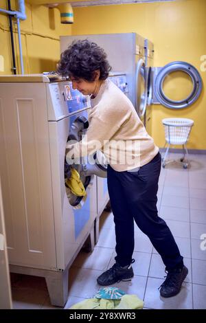 una giovane donna di grandi dimensioni carica i vestiti in una lavatrice in una lavanderia nel seminterrato di un dormitorio studentesco Foto Stock