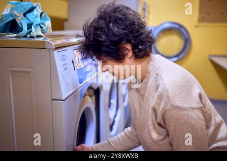 una giovane donna di grandi dimensioni carica i vestiti in una lavatrice in una lavanderia nel seminterrato di un dormitorio studentesco Foto Stock