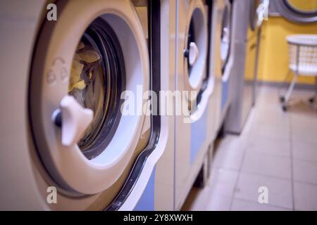 una giovane donna di grandi dimensioni carica i vestiti in una lavatrice in una lavanderia nel seminterrato di un dormitorio studentesco Foto Stock