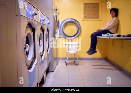 una giovane donna di grandi dimensioni carica i vestiti in una lavatrice in una lavanderia nel seminterrato di un dormitorio studentesco Foto Stock