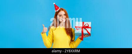 Girovita-su colpo soddisfatto buon-sguardo redhead donna che mostra pollice-in su nell'approvazione o come, amore che celebra le feste di natale e riceve i regali Foto Stock