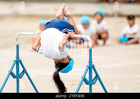 Una ragazza giapponese in uniforme da P.E. che fa ginnastica al bar di un evento sportivo scolastico giapponese Foto Stock