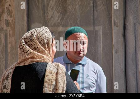 Samarcanda, Uzbekistan; 18 settembre 2024: Una donna con un velo tradizionale e un uomo con un berretto uzbeko, in piedi faccia a faccia nella storia Foto Stock