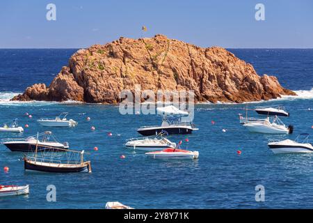 Vista pittoresca delle barche nella baia blu che galleggiano vicino all'isola rocciosa nelle acque costiere di Tossa de Mar, Spagna, Catalogna Foto Stock