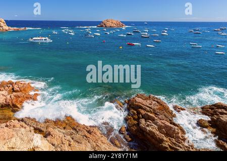 Vista pittoresca delle barche nella baia blu che galleggiano vicino all'isola rocciosa nelle acque costiere di Tossa de Mar, Spagna, Catalogna Foto Stock