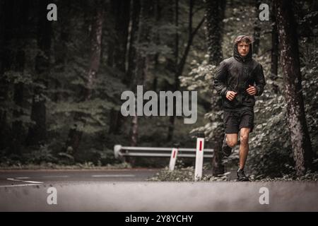 Un giovane corridore maschile si allena per una partita di calcio, correndo su una strada asfaltata in autunno Foto Stock