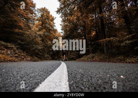 Colpo largo di un atleta maschile non riconosciuto che corre su una strada asfaltata in autunno Foto Stock