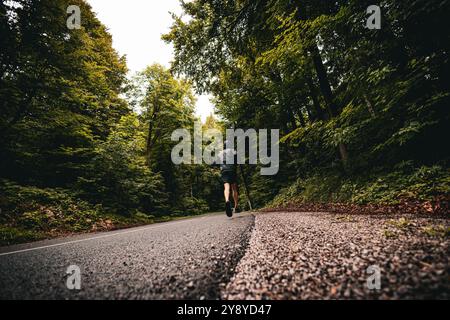 Uomo atletico non riconosciuto che corre su una strada asfaltata. Da dietro le quinte. Foto Stock