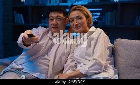 Coppia multirazziale guardare film di sera diverse sposate asiatico uomo e donna caucasica famiglia felice multietnico coreano marito e moglie Foto Stock