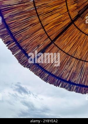 ombrellone di paglia sulla spiaggia contro il cielo nuvoloso, concetto minimale, consistenza. Foto di alta qualità Foto Stock