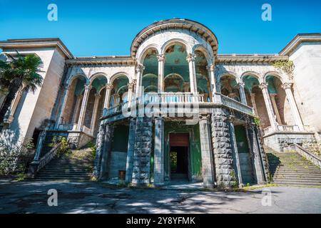 Facciata del sanatorio Medea abbandonato a Tskaltubo, Georgia. L'architettura neoclassica con alte colonne e grandi archi mostra segni di decadimento, circondato dalla natura. Foto Stock