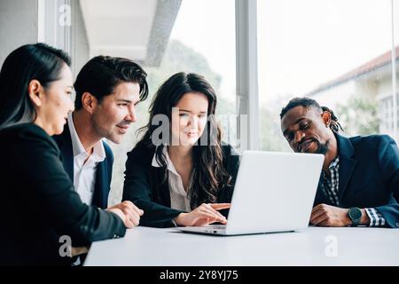 In una sala riunioni diversi team di uomini e donne collaborano con un computer portatile. Loro Foto Stock