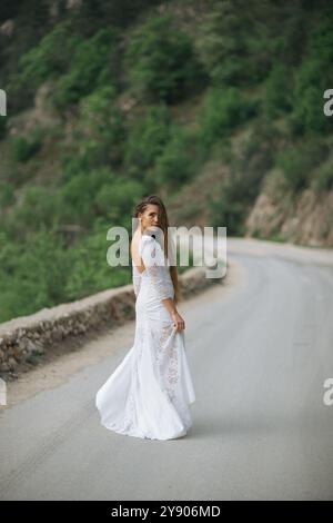 Una donna con un vestito bianco è in piedi su una strada. La strada è vuota e la donna è l'unica persona sulla scena. Foto Stock