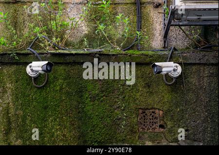 Due telecamere di sicurezza a circuito chiuso che si guardano e si guardano su un muro esterno Foto Stock