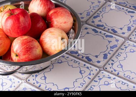 Le mele rosse giacciono in un colorante metallico su un tavolo con una superficie piastrellata blu e bianca Foto Stock