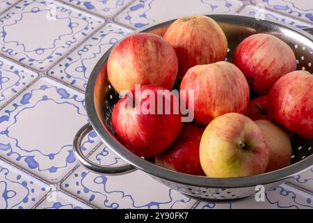 Le mele rosse giacciono in un colorante metallico su un tavolo con una superficie piastrellata blu e bianca Foto Stock