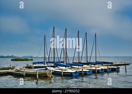 Piccole barche a vela ormeggiate in un molo di legno in un lago in una giornata ventosa. Leekstermeer, provincia di Groninga, Paesi Bassi Foto Stock