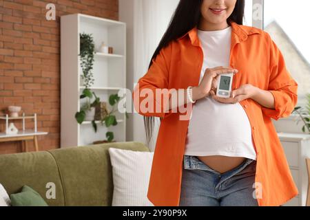 Giovane donna incinta con diabete gestazionale e glucometro a casa Foto Stock