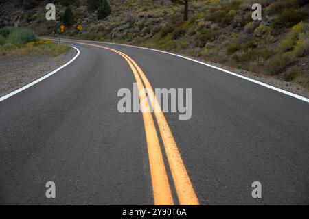 Doppie linee gialle, curva in discesa davanti alla strada di montagna. Foto Stock