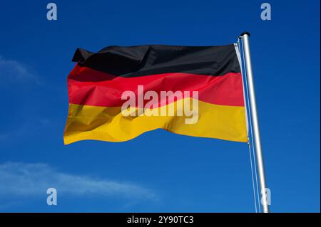 La bandiera della Germania fluttua nel vento contro un cielo azzurro senza nuvole Foto Stock