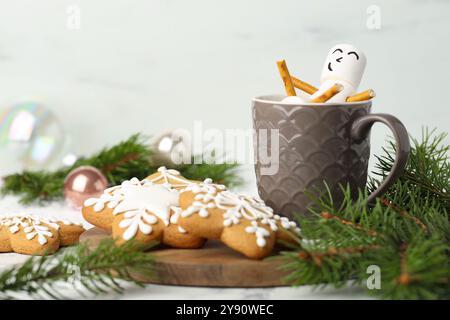 Simpatico pupazzo di neve marshmallow in tazza di bevanda calda e biscotti al pan di zenzero su un tavolo bianco con arredamento natalizio Foto Stock