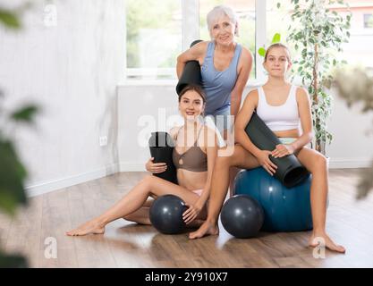 Tre donne di età diverse in abbigliamento sportivo che posano insieme nello studio di yoga Foto Stock