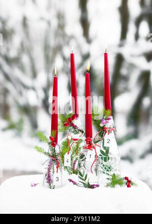 Corona dell'Avvento con quattro candele rosse e pendenti bianchi in legno in bottiglie di vetro decorate con rami di abete. Foto Stock