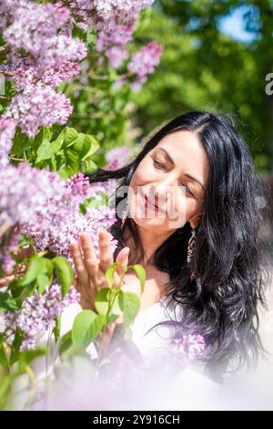 Lady Relishing Aroma of Lilac Blossoms in Bright Sunlight within Flourishing Garden, concetto di relax Foto Stock