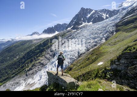 Alpinista in piedi su una roccia, paesaggio di montagna con ghiacciaio dei Bossons e cima dell'Aiguille du Midi, Chamonix, alta Savoia, Francia, UE Foto Stock