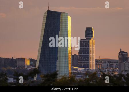 La luce del sole tramonta lateralmente sulla facciata in vetro della Banca centrale europea (BCE) e della Torre Henninger a Francoforte sul meno, lo Foto Stock