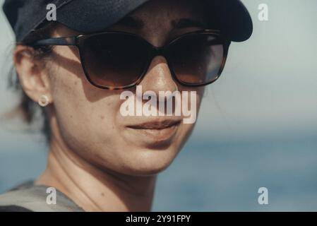 Donna con occhiali da sole e berretto che guarda in lontananza con il mare sullo sfondo Foto Stock