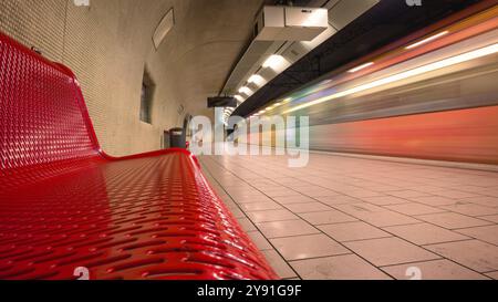 Moderno letto ferroviario sotterraneo con panca rossa e treno di passaggio ad alta velocità Foto Stock