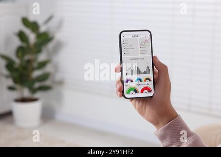 Uomo che monitora le letture dei contatori intelligenti sul telefono cellulare a casa, primo piano Foto Stock