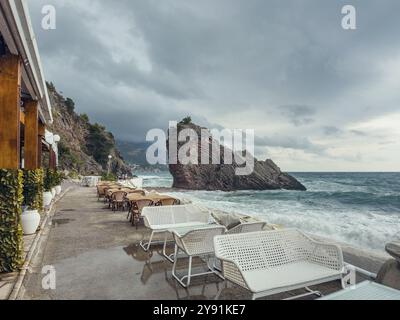 Caffetteria sulla spiaggia vuota durante la giornata nuvolosa con grande roccia nel mare, Rafailovici, Montenegro Foto Stock